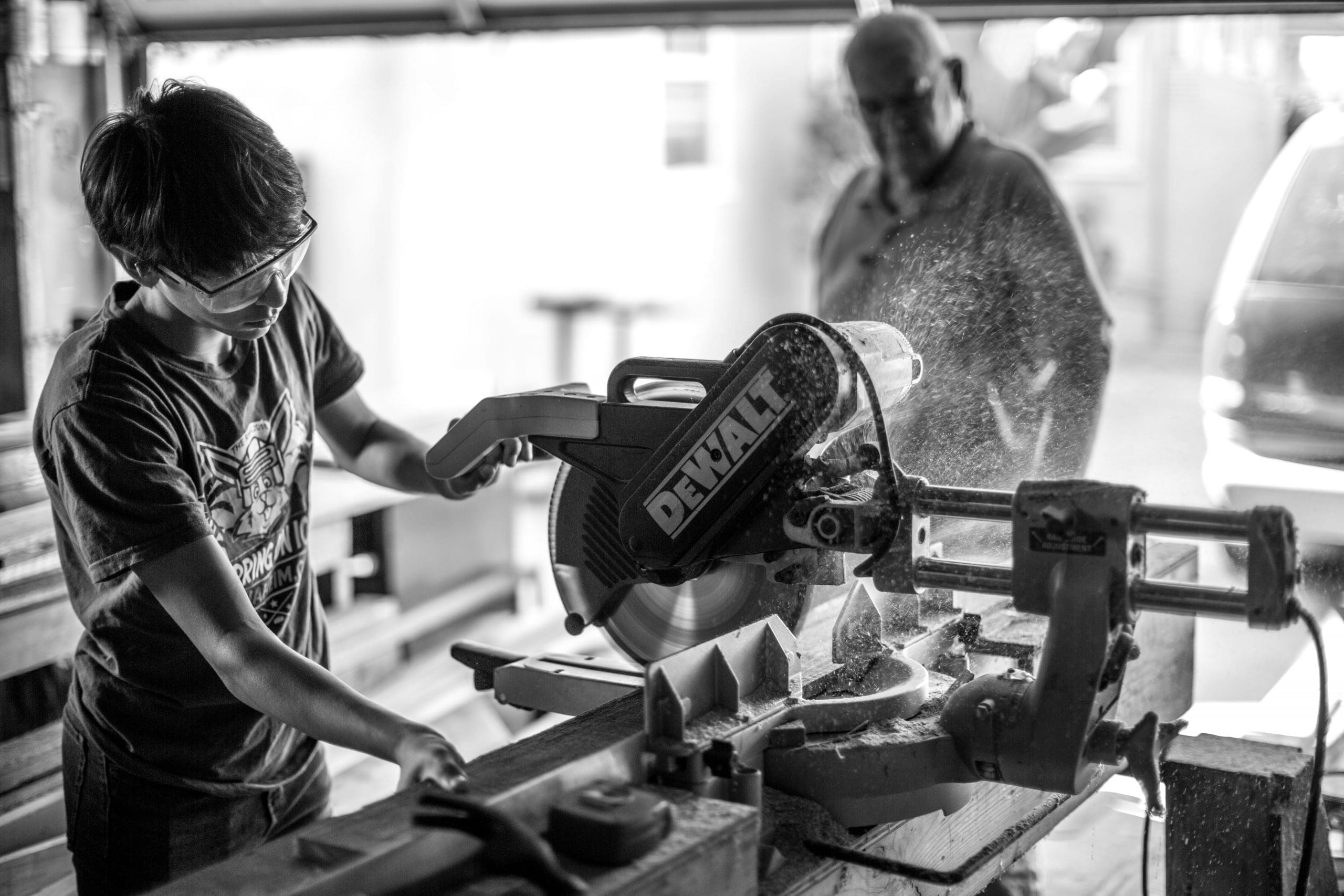 power saw grayscale photography of boy using miter saw