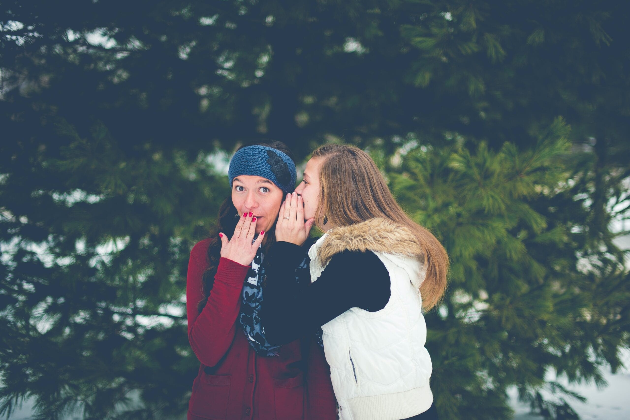 woman whispering on woman's ear while hands on lips Grapevine Communication