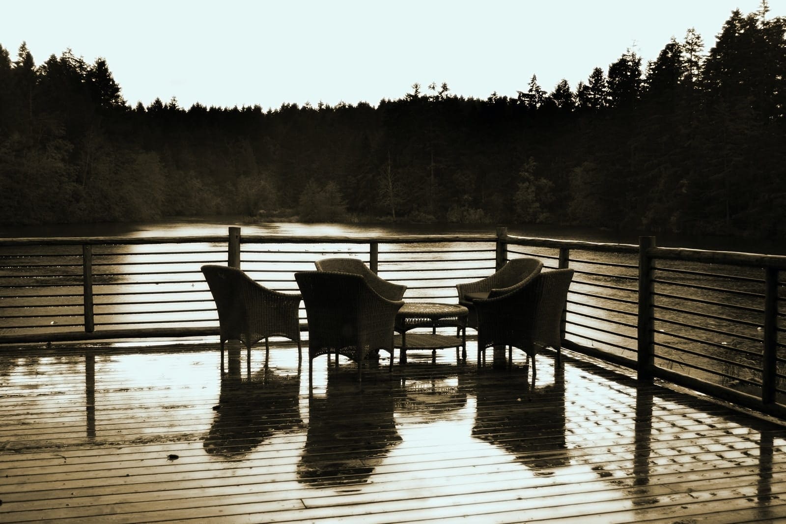 grayscale photo of two wooden chairs on wooden dock deck by the river