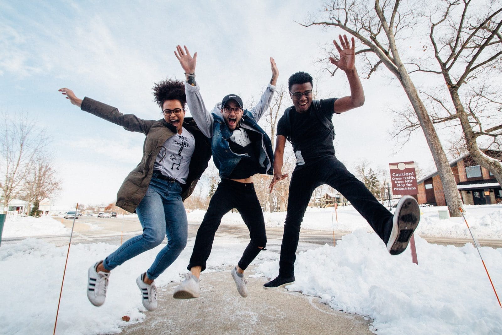 college photo of three men jumping on ground near bare trees during daytime