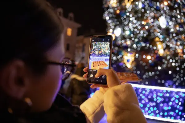 person holding iphone taking photo of lighted christmas tree