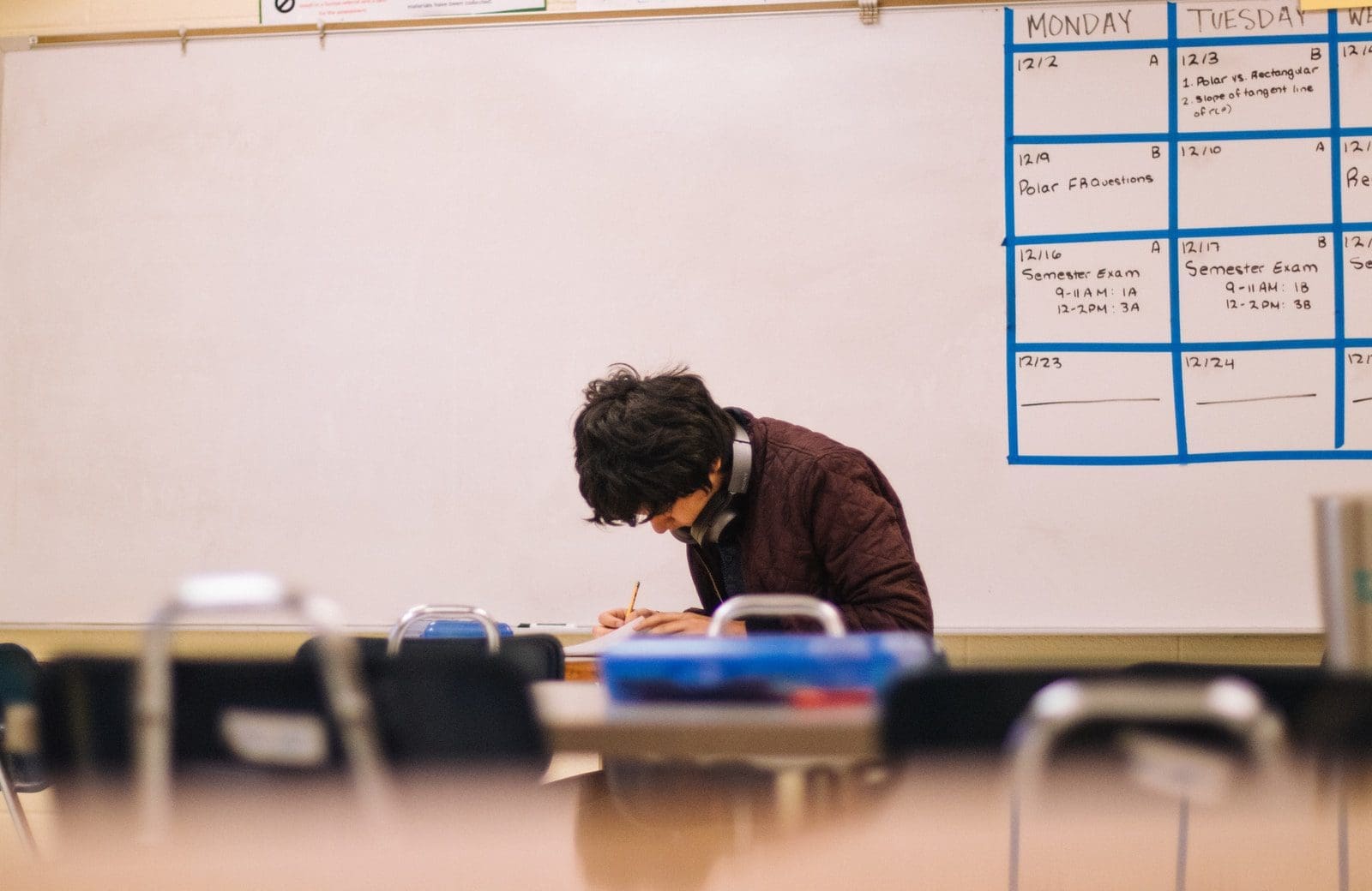 man in brown sweater sitting on chair writing exam