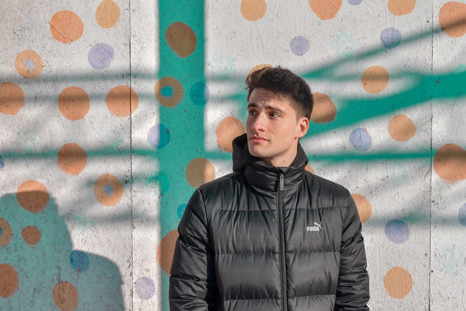 man wearing black zip-up jacket standing beside white and red polka-dot wall