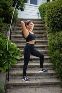 woman in black sports bra and black pants standing on gray concrete stairs