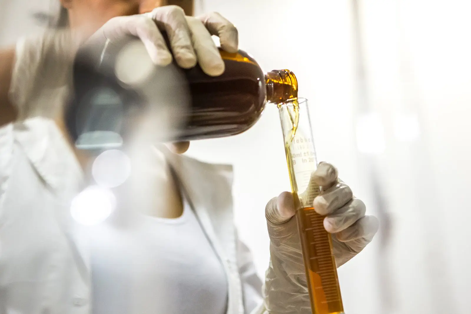 pharmaceutical scientist woman wearing white lab coat holding brown bottle and glass tube