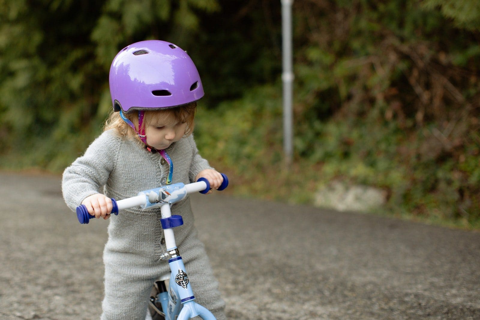 road safety Cute toddler child wearing protective helmet and warm bodysuit playing with bicycle on road near green plants on rural street
