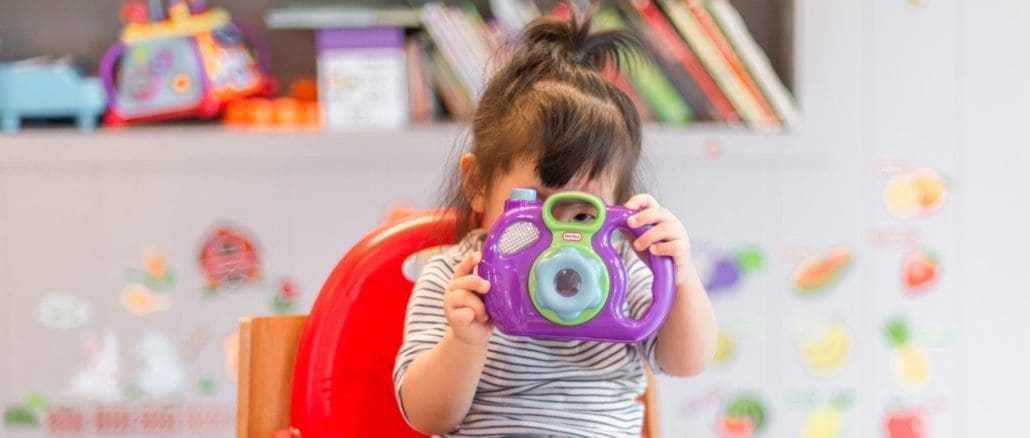 girl holding purple and green camera toy baby-proofing your home