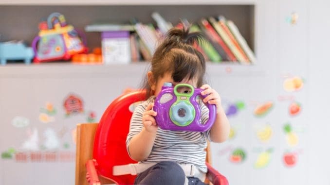 girl holding purple and green camera toy baby-proofing your home