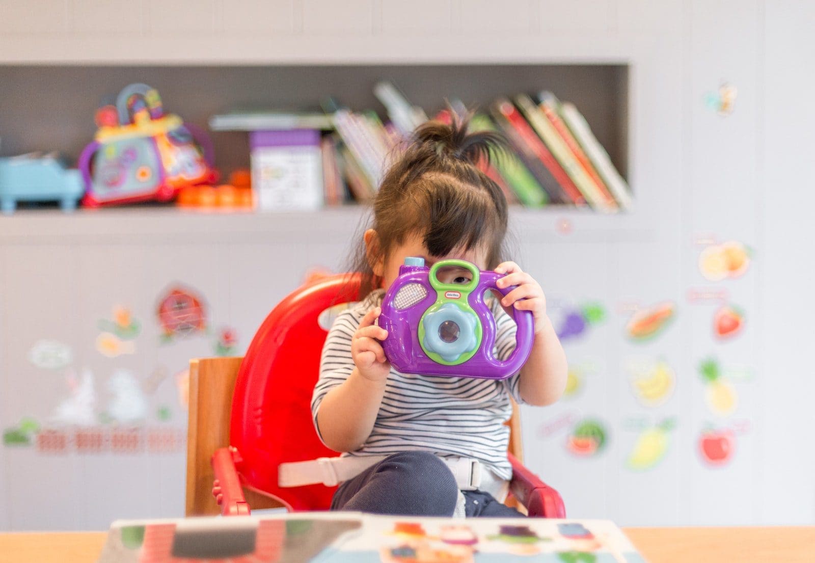 girl holding purple and green camera toy baby-proofing your home
