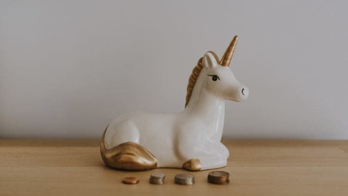 white and gold ceramic unicorn figurine near coins gold and silver
