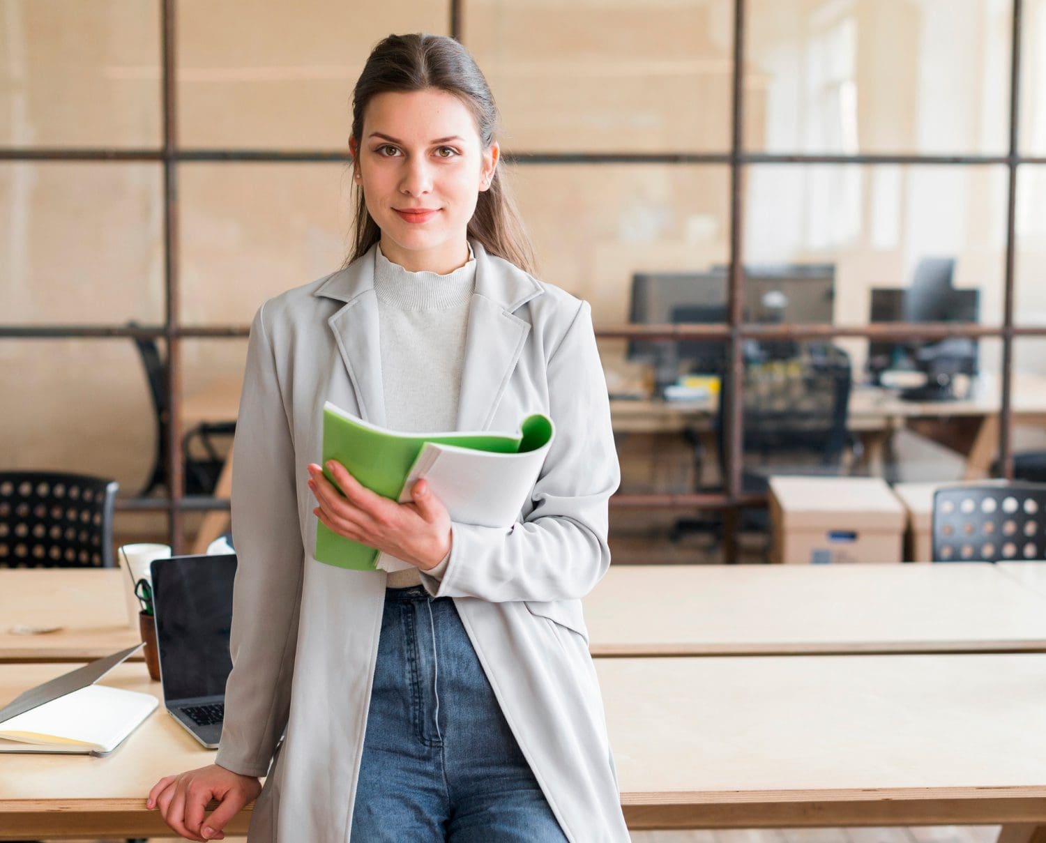 pretty young businesswoman leaning desk holding book looking camera office