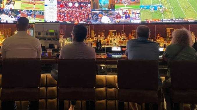 a group of people sitting at a bar watching tv sports betting