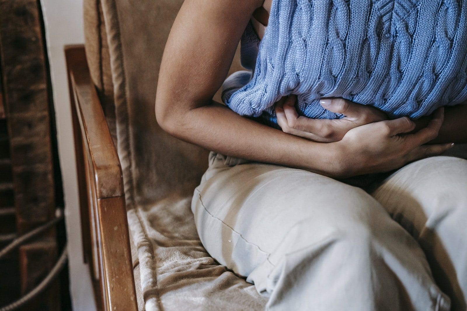 Crop unrecognizable female touching belly while having acute pain in stomach sitting on couch