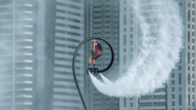 man in orange jacket riding bicycle on white water wave during daytime dubai with friends