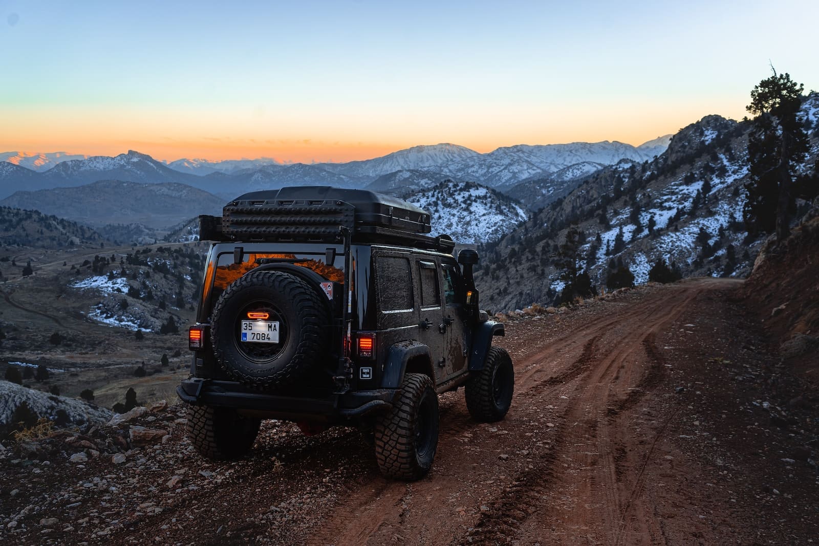 a jeep driving down a dirt road with mountains in the background