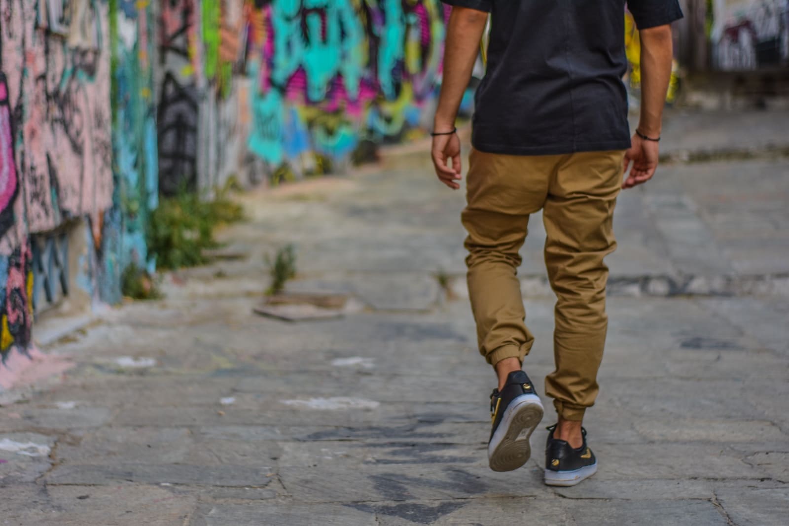 Ultimate Guide To Selecting Men'S Pants 2 man wearing black shirt and brown men's pants walking beside wall with graffiti