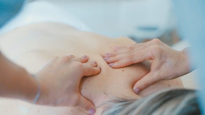 person massaging the back of a woman physiotherapy at home