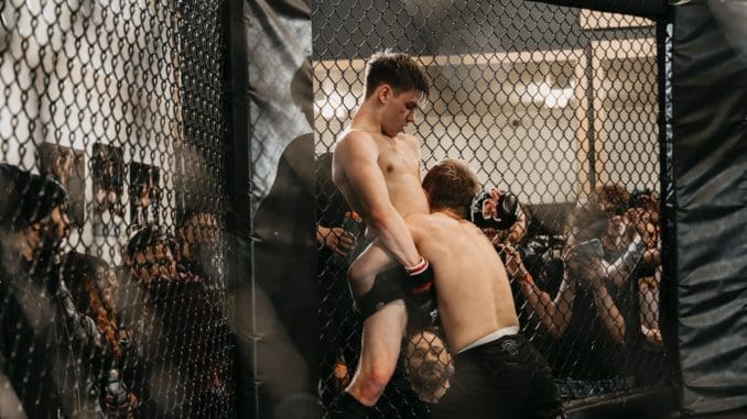 a couple of men standing next to each other in a cage mma betting