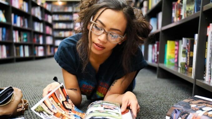 woman in black, blue, and red shirt lying on surface while reading magazine