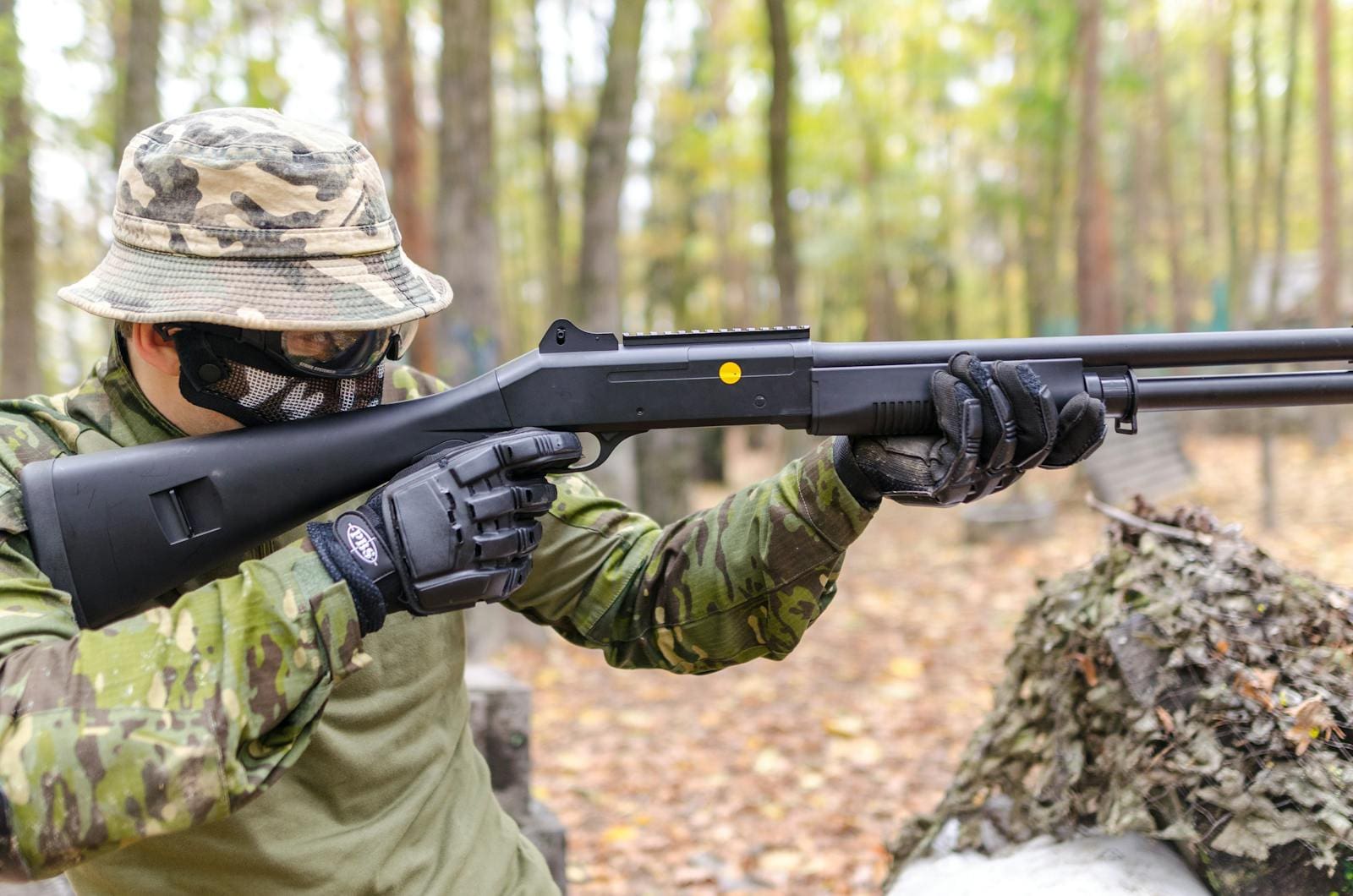 Man in camouflage aiming an airsoft rifle outdoors, highlighting combat training.